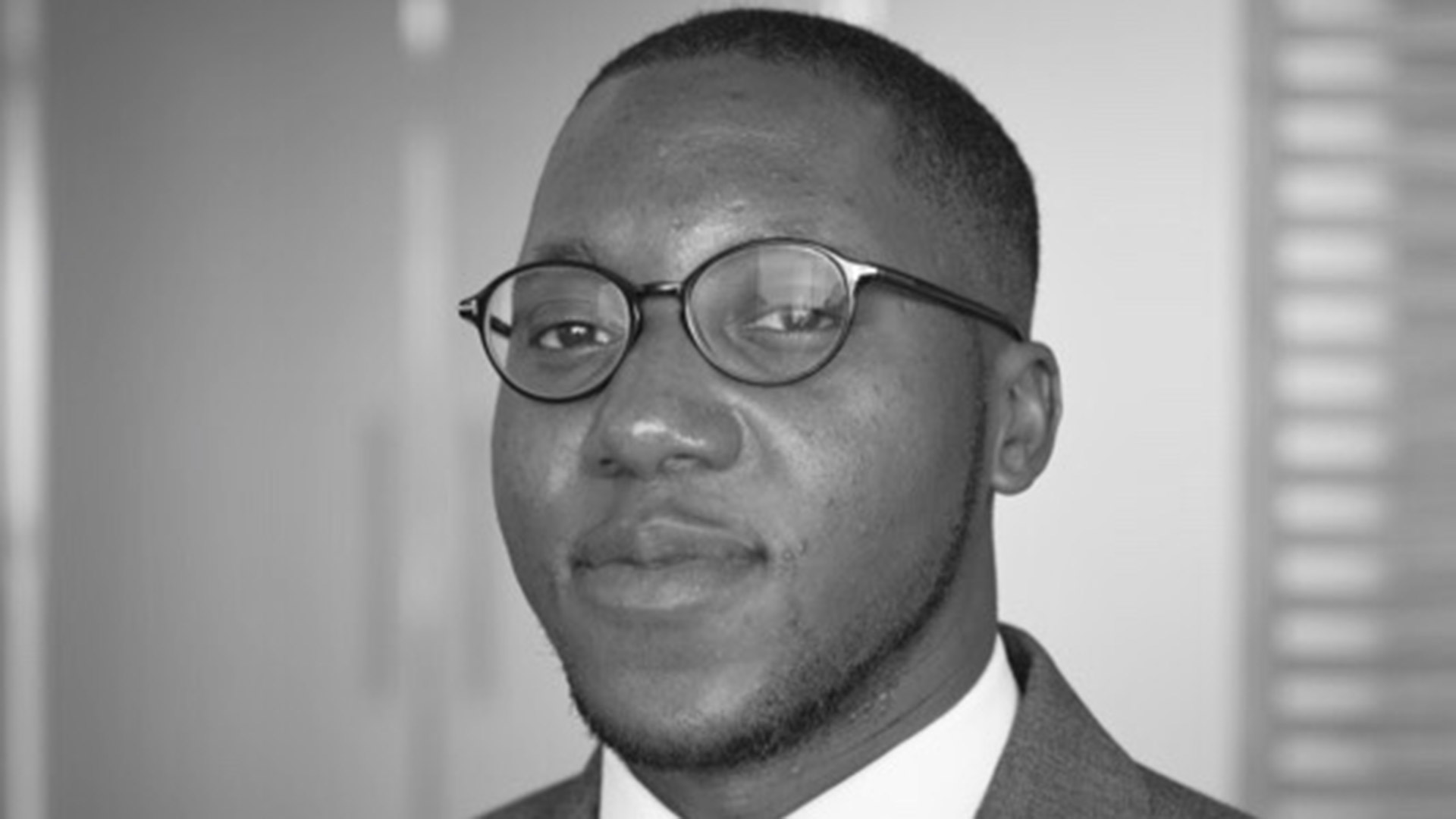 A black and white headshot photo of a man wearing glasses and a suit and tie.